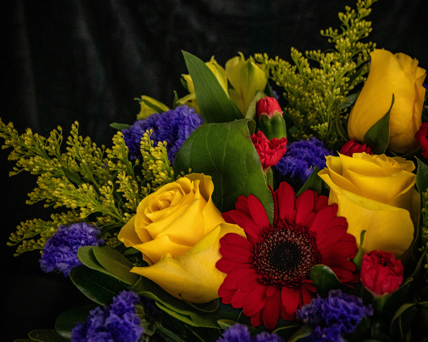 Bouquet of yellow roses, red daisies, and purple flowers on a black background